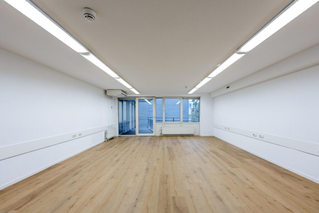 Leeg, wit kantoorpand met houten vloer en grote ramen aan de Prins Hendrikkade.